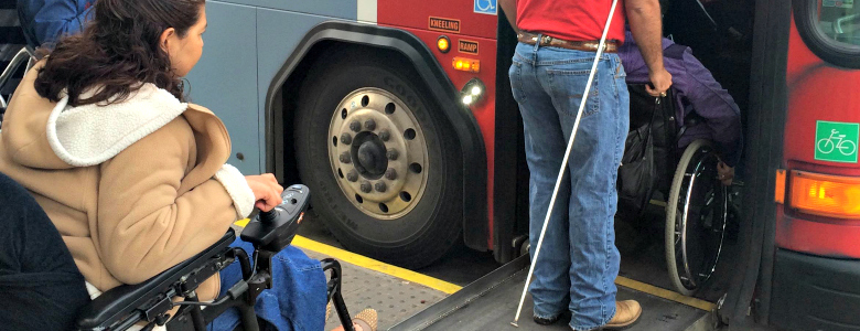 Woman in wheelchair being assisted onto bus.